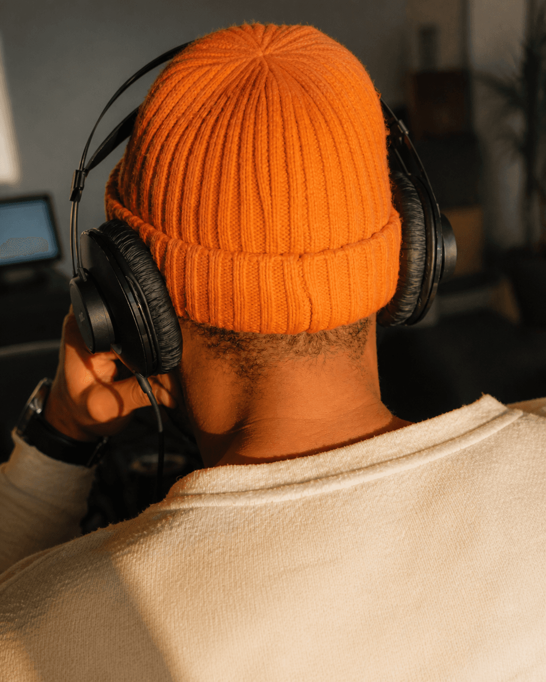 A person in an orange knit beanie wearing studio headphones.